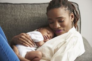 Black mother cuddling sleeping baby son on sofa