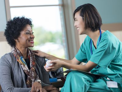 Friendly Asian nurse or doctor giving medication to patient