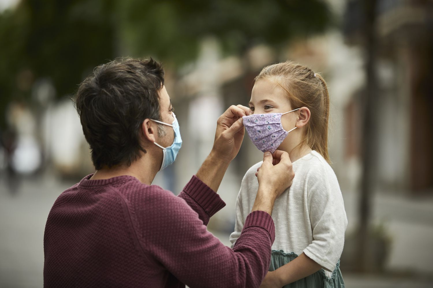 man helping little girl put on her face mask.