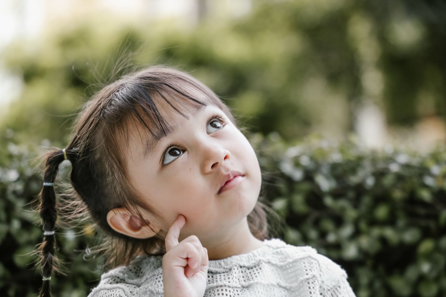 Little girl outside with pigtails looking up and thinking.