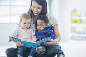 一个保姆拿着一本书给两个小孩读书
