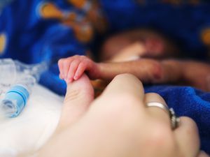 早产儿男婴(0-3个月)在保温箱中，握着妈妈的大拇指