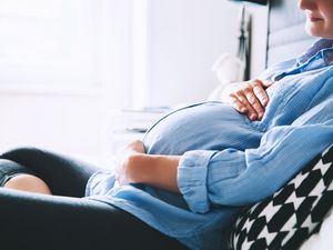 孕妇坐在床上，手放在肚子上的卧室在家里。