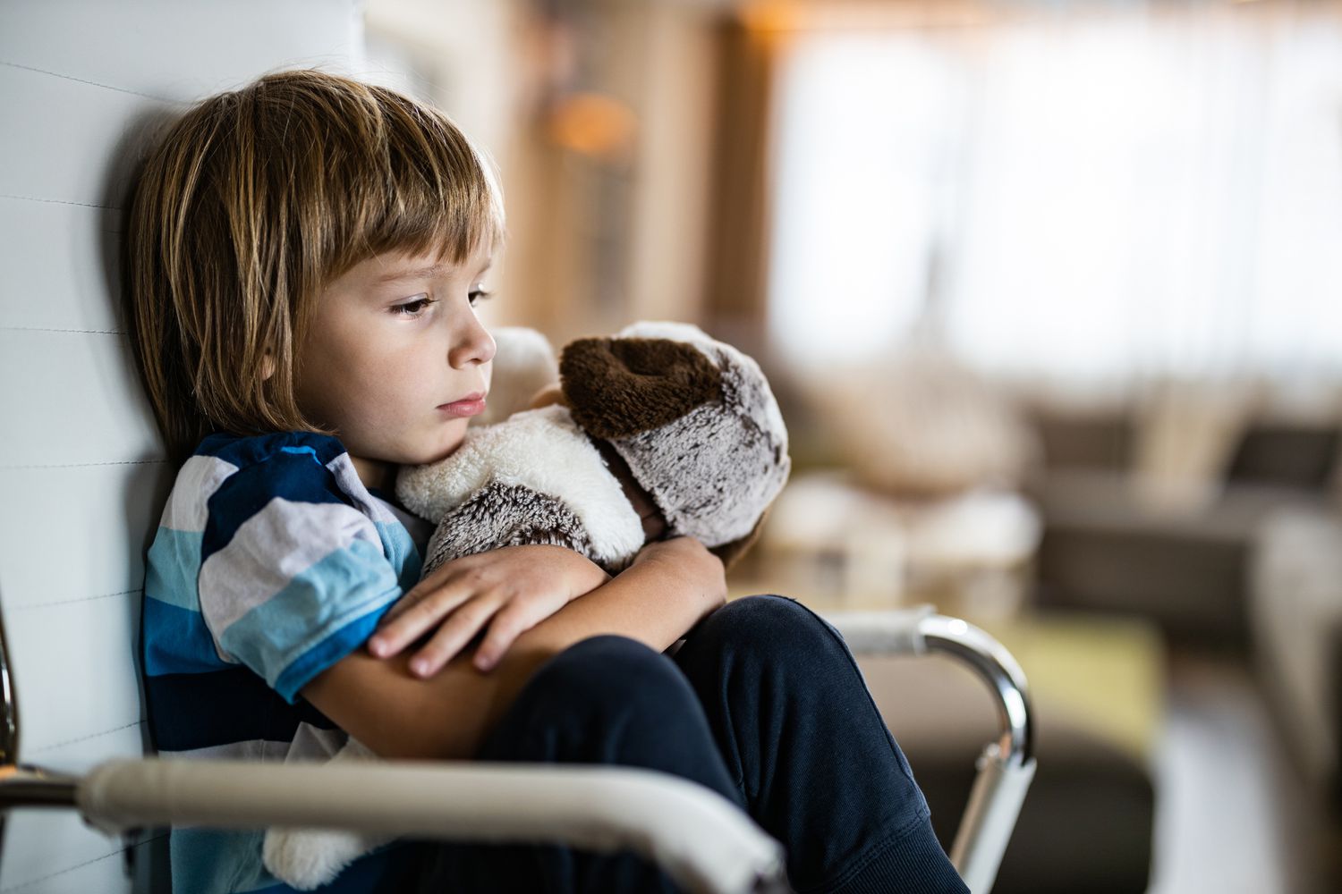 Sad boy embracing his teddy bear in home isolation.