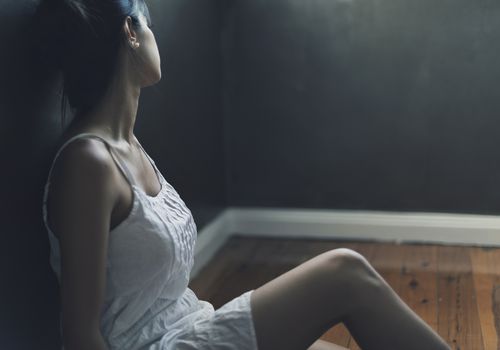 沮丧的女人坐在地板上，靠在墙上