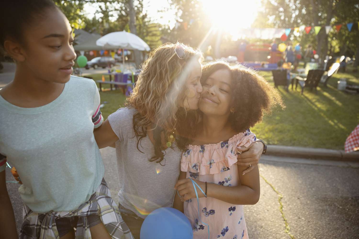 Affectionate mother kissing daughters cheek at summer neighborhood block party in park