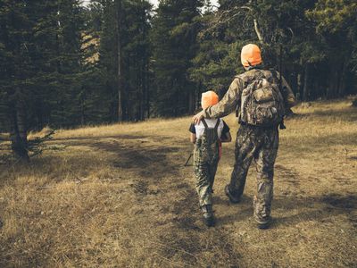 Grandfather and grandson hunters in camouflage bonding, walking in woods