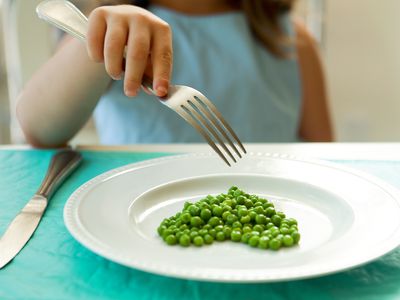 Girl eating green peas with a fork.
