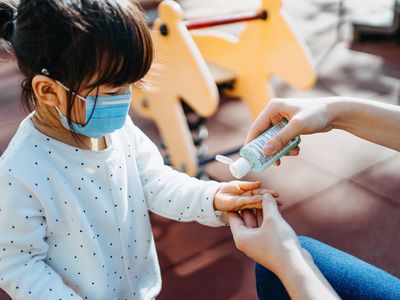 Child in mask applies hand sanitizer