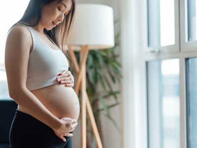Pregnant person gazes down at pregnant belly.