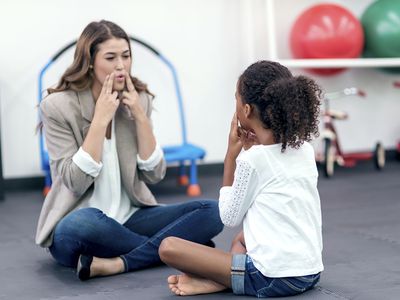 Adult female therapist guiding young girl in speech therapy