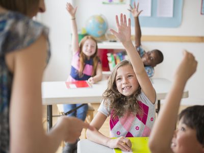 Children (8-9) raising hands in classroom