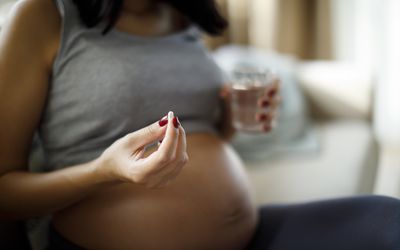 Pregnant woman holding a white pill and a glass of water