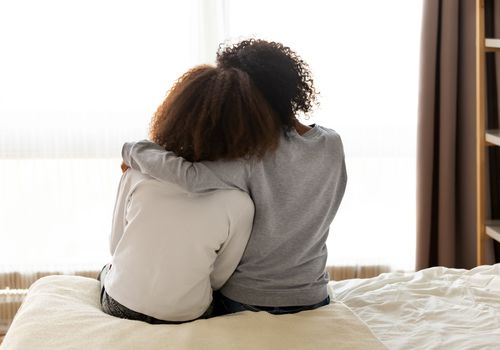 Rear view of mother and daughter sitting on bed