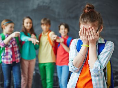 girl covering her face with bullies in background