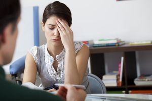 女人双手抱头，隔着桌子和医生说话