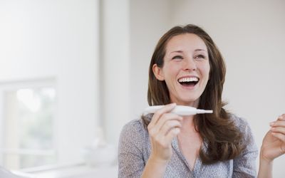a smiling woman holding a positive pregnancy test