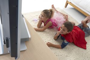 two children watching tv while wearing Halloween costumes