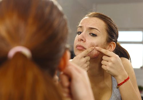 woman popping pimple in mirror