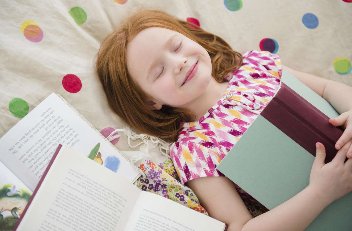 Young girl laying down and smiling with a book on her chest