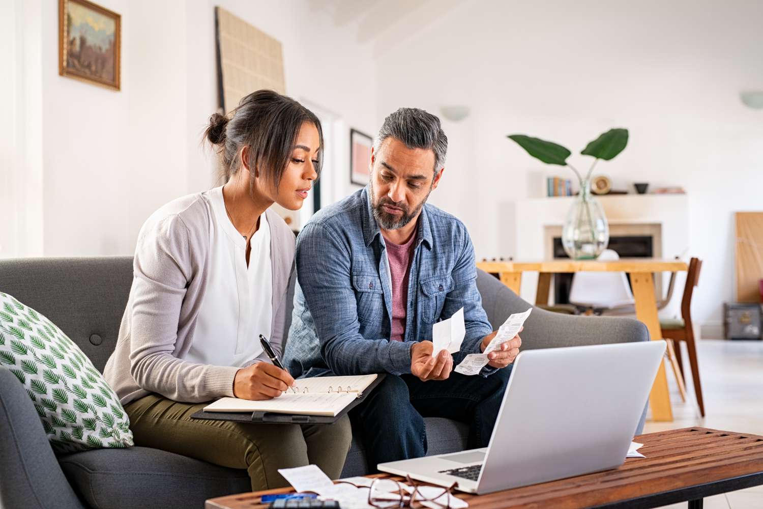 Couple calculating bills at home using laptop and calculator.