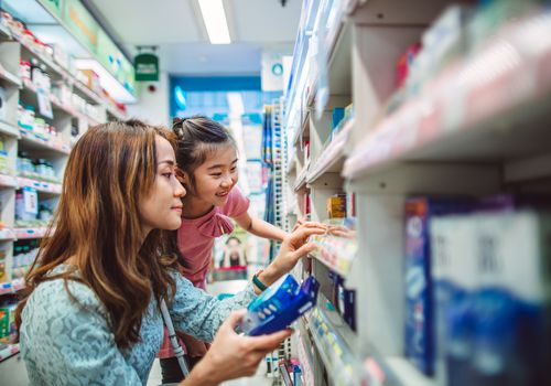 Asian woman and child crouching down at the drugstore examining medicine.