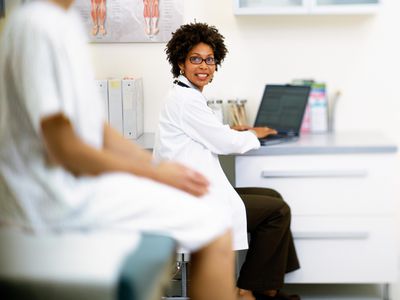 Female doctor talking to patient and using laptop in exam room, discussing IUI procedure