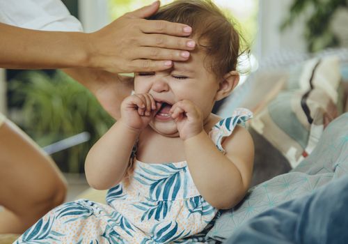 Mother holding her hand to the forehead of her crying baby girl