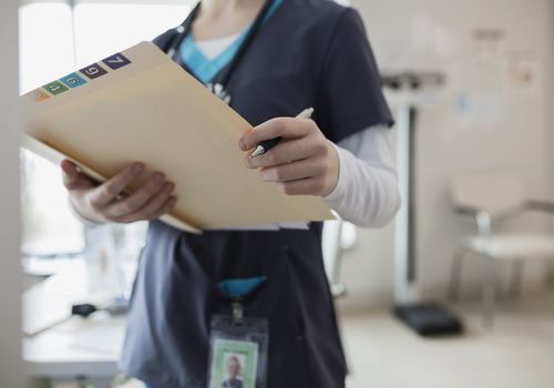 Nurse in scrubs holding medical chart in clinic