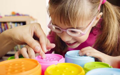 Smiling child with disability touching textured cups with her teacher