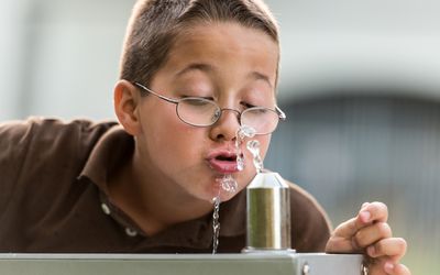 男孩在学校的喷泉喝水。