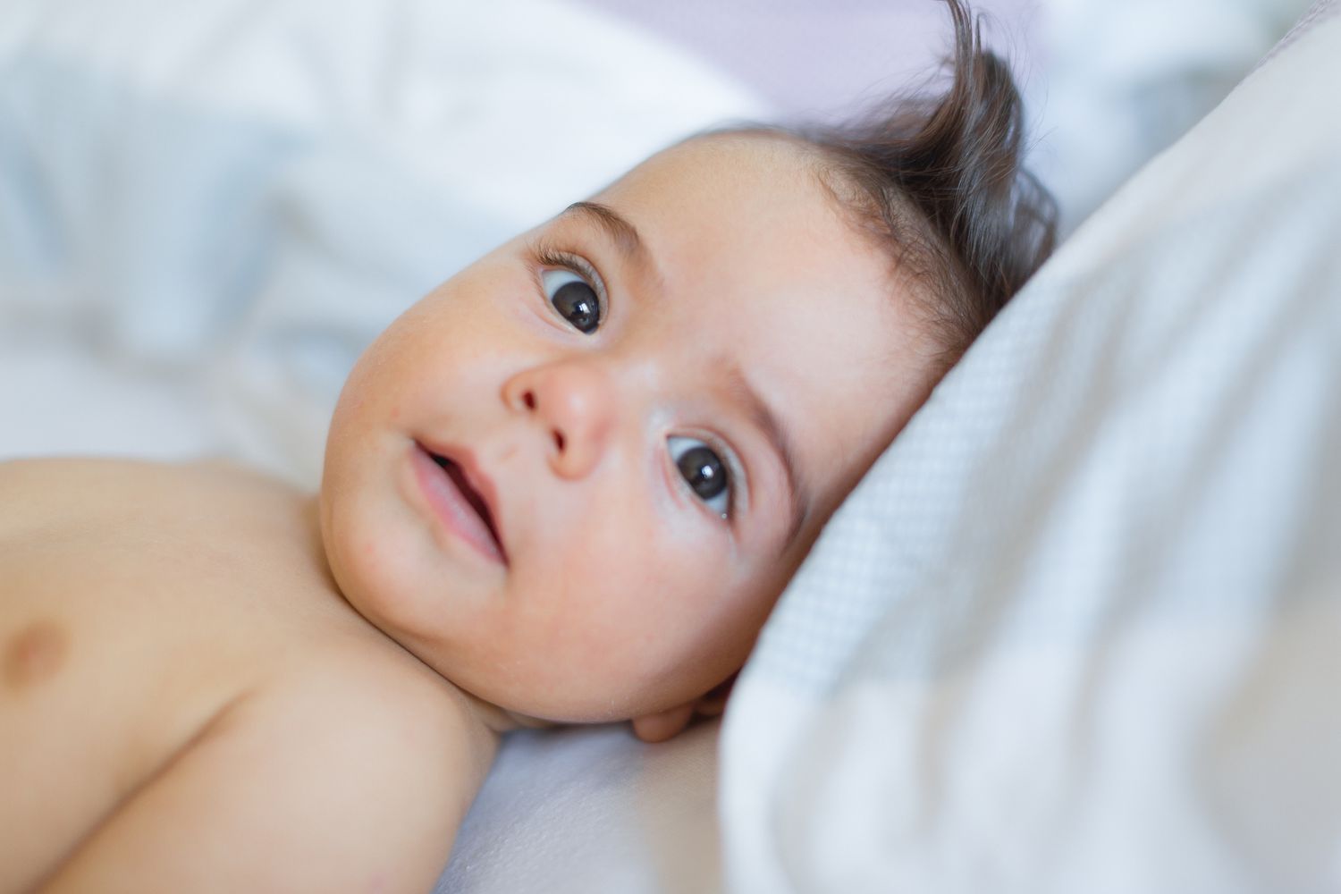 Baby boy laying on white bed looking at camera