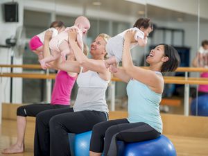 妇女们在健身课上把婴儿抱在健身球上。