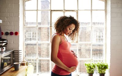 A pregnant woman holds her bump in kitchen window