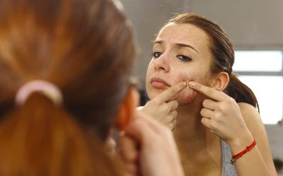 woman popping pimple in mirror