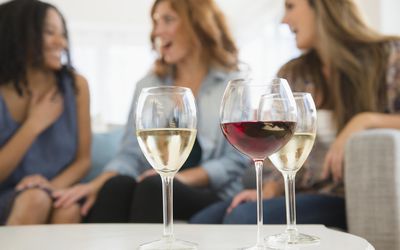 Women drinking wine and talking on sofa in living room