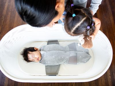 Person and child looking over a baby sleeping in the SNOO Smart Sleeper Bassinet
