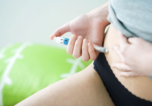 Person with light skin gives injection into their abdomen