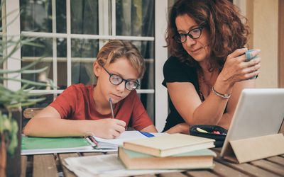 年轻的学生在家里用学校的书、报纸、数码板做作业，由母亲帮助。母亲控制、帮助和教育儿子。教育，家庭，生活方式和在家上学的概念。