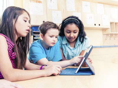 Two girls and one boy using tablet in classroom