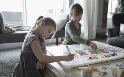 Sisters making chore list on whiteboard in living room