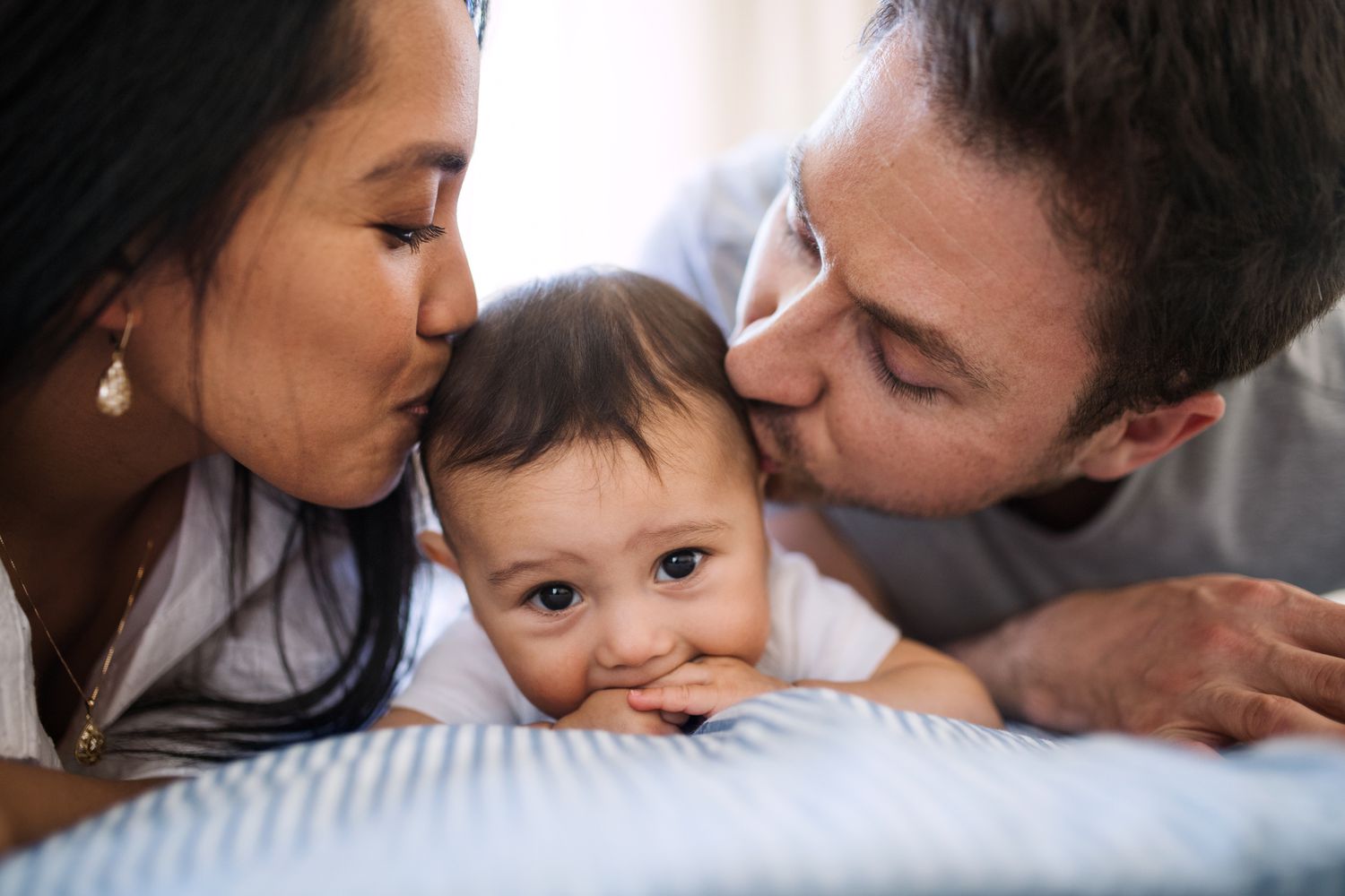 热情洋溢的年轻夫妇抱着一个婴儿在家里的床上休息。