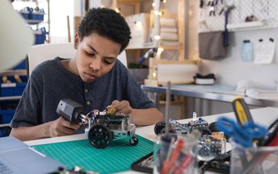 Teen boy solders wires to build robot
