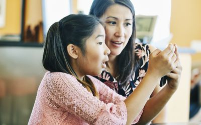 mother and daughter making video call on smart phone at kitchen table