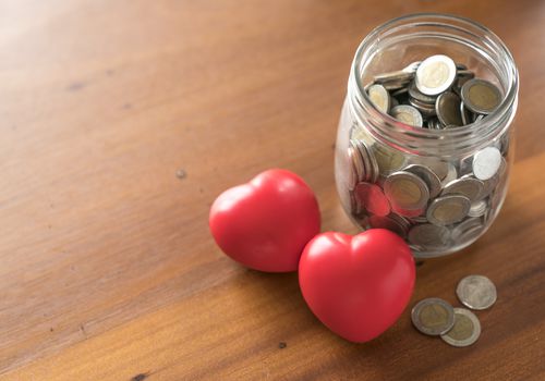 Red toy hearts next to a jar of coins
