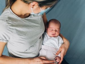 New mom holding baby wearing a mask
