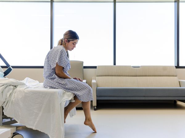 Sad young adult woman waits for doctor in hospital gown