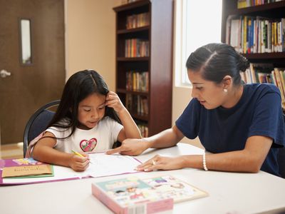 Hispanic woman helping girl with homework in library