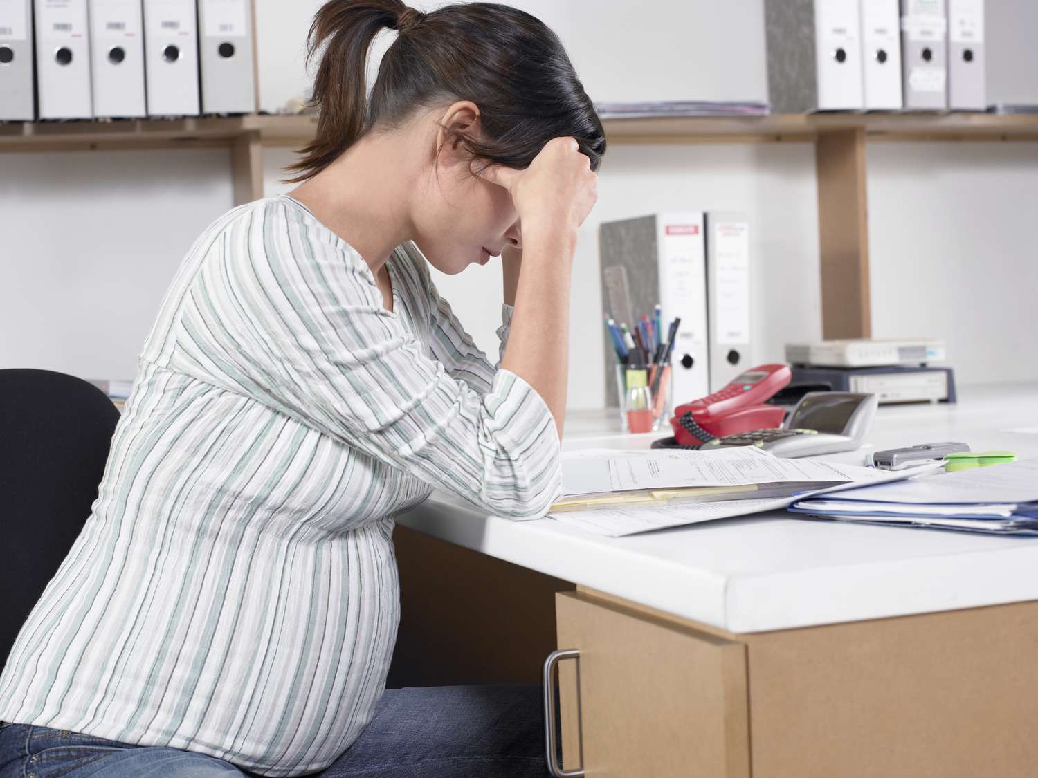 A pregnant women at her desk, head in hands.