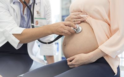 Doctor using stethoscope on pregnant patients stomach
